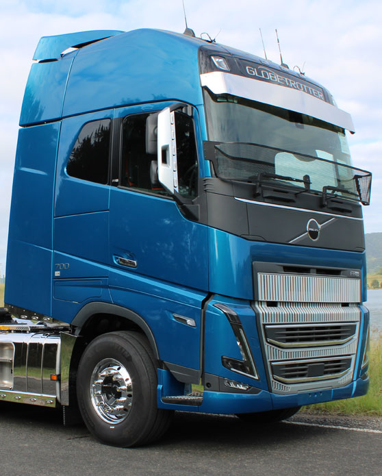 A blue Volvo semi-truck cab is parked on the roadside, featuring chrome wheels and the distinctive Volvo Globetrotter logo above the windshield.