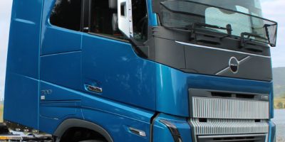 A blue Volvo semi-truck cab is parked on the roadside, featuring chrome wheels and the distinctive Volvo Globetrotter logo above the windshield.
